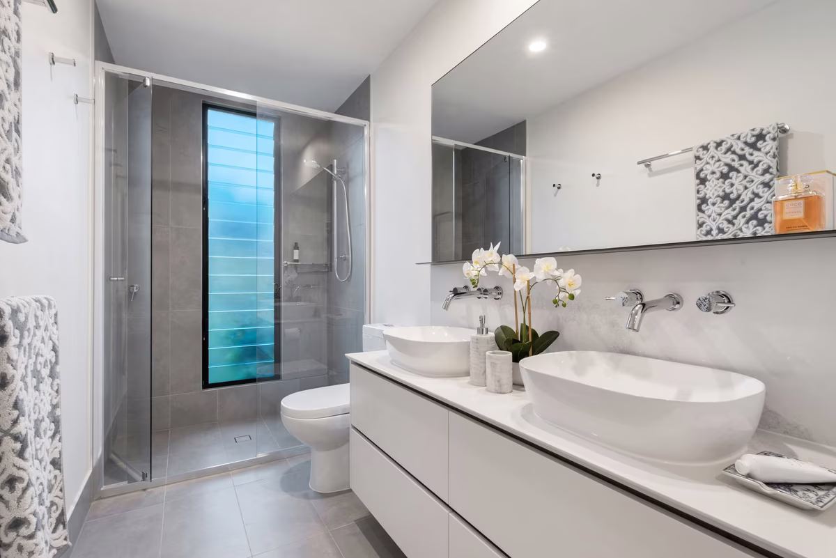 Modern bathroom with blue glass window feature, white vessel sinks, and grey tile accents