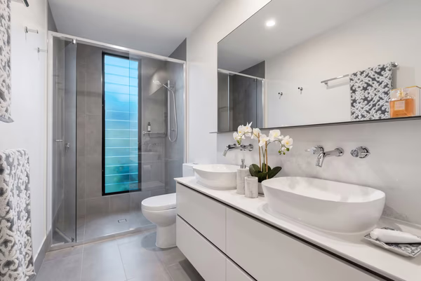 Modern bathroom with blue glass window feature, white vessel sinks, and grey tile accents