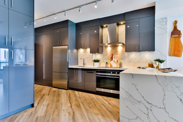 Modern two-tone kitchen with marble waterfall countertop and track lighting