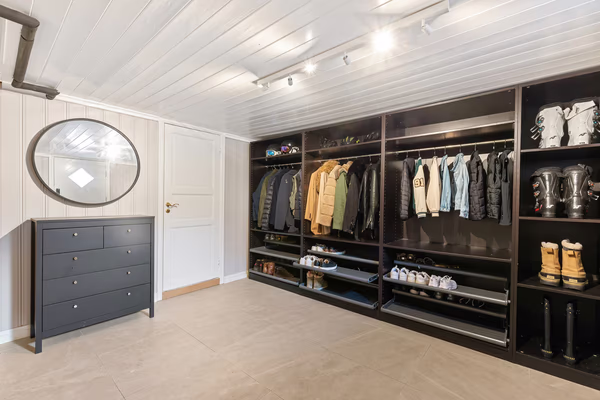 Modern walk-in wardrobe with dark storage units and grey dresser